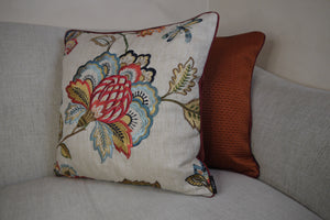 Hazeldee Home Limited Edition Handmade double-sided cushion using the luxurious Colefax and Fowler heavily embroidered floral foliage design fabric on a linen/viscose base on one side and Italian velvet terracotta on the reverse, edged with satin trim.   The front features an intricate floral design reminiscent of a tudor floral design with hues of rust, gold, navy light and mid blues on a linen blend neutral base with a subtle herringbone semi-plain weave that adds dimension depth and interest.  